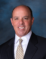 Headshot image of Donn Lux wearing a blaack suit jacket and gold tie while smiling.