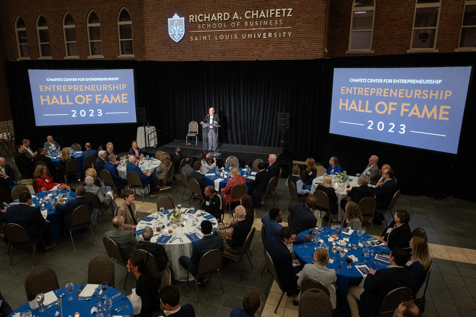 Dinner participants sit at round tables in a banquet room with two screens at the front that read Entrepreneurship Hall of Fame 2023