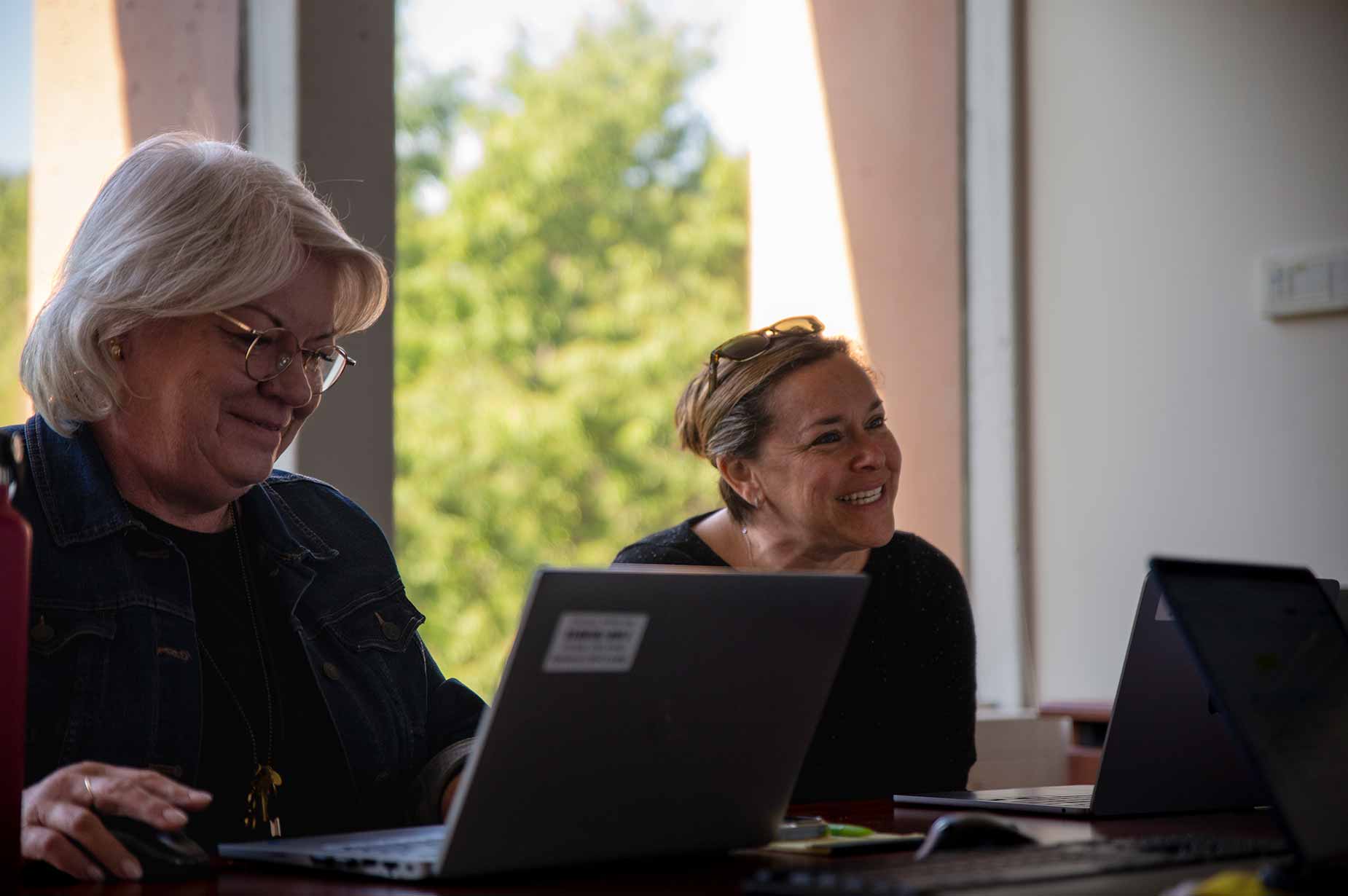 A SLU female faculty member looks over a folder with a SLU student. They are standing in the hallway of an elementary school and other SLU students can be seen in the background.