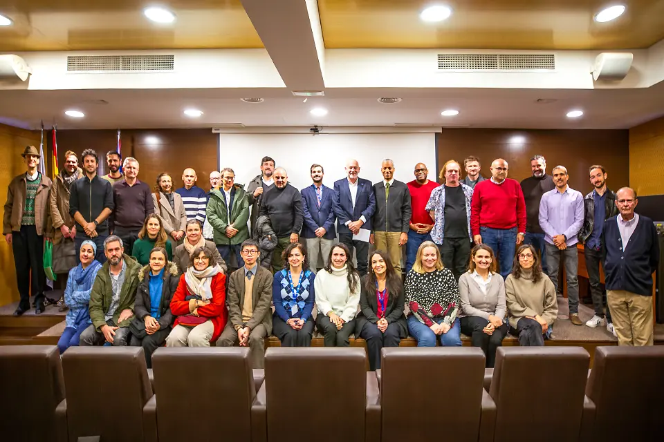 Faculty members pose while standing and sitting on the podium in an auditorium.