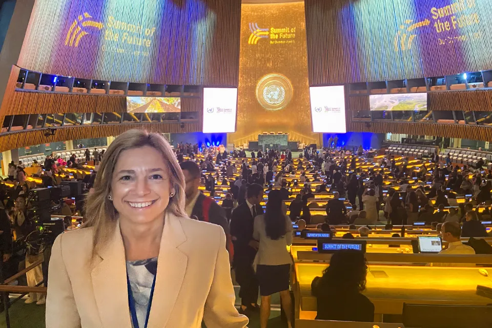 Woman smiles at camera in front of meeting space at the UN's headquarters.