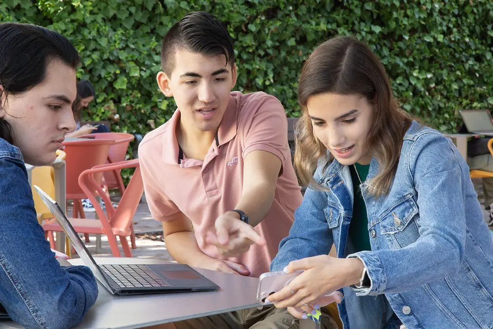 Students with a laptop looking at a phone in the patio of PRH.