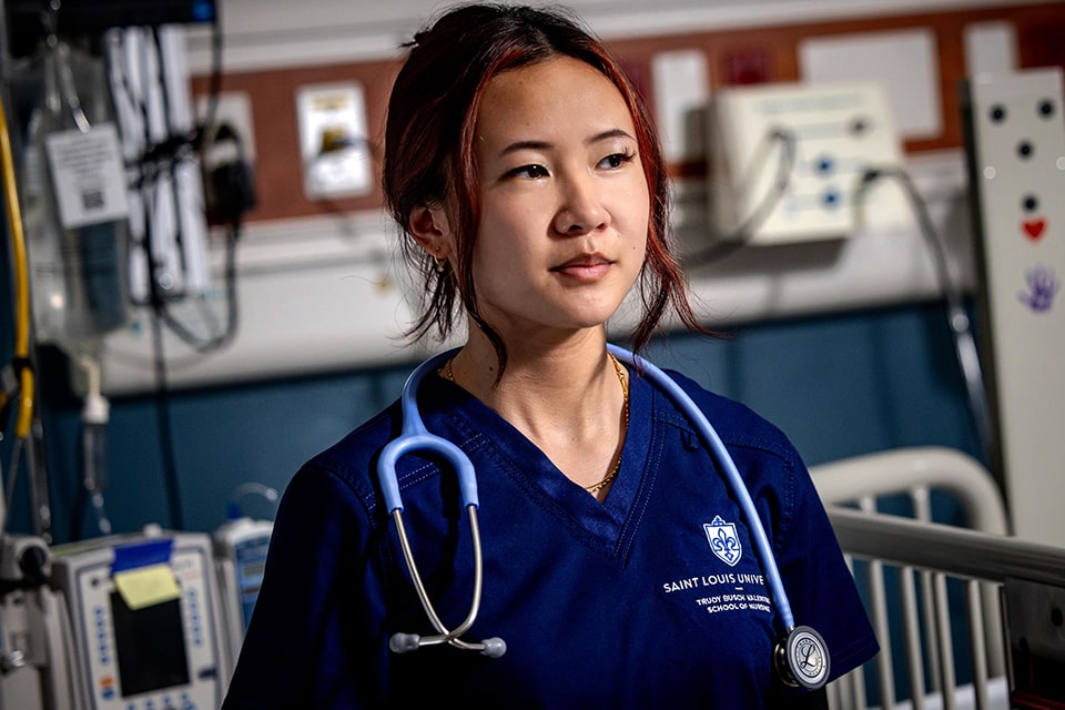 A student wearing nursing school scrubs stands in a clinical area with a stethoscope around her neck.