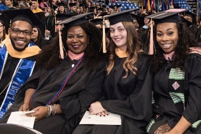 4 slu graduates wearing caps and gowns sitting at commencement ceremony