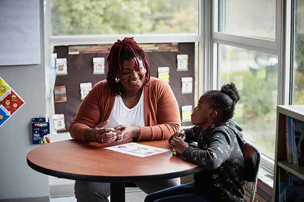 A female SLU student talks with a young girl at a round table in a classroom.