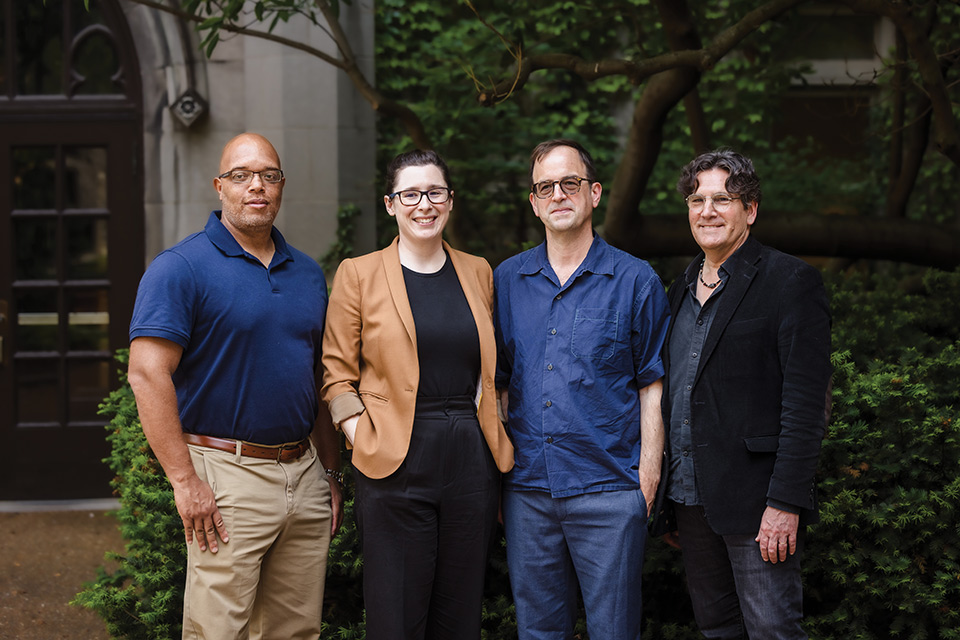 From left, a bald Black man wearing a navy polo shirt and khakis stands next to a white woman wearing black pants and a shirt, and a camel blazer. To her left are two white men, one wearing all dark blue, and the other in a black jacket.