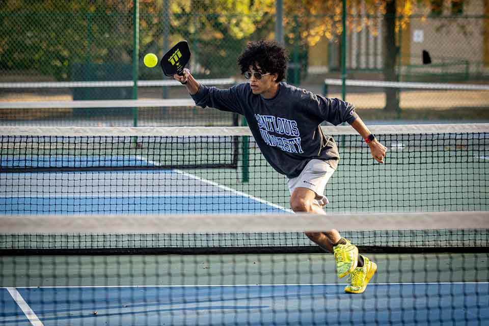 A male pickleball player hits the ball on a court.