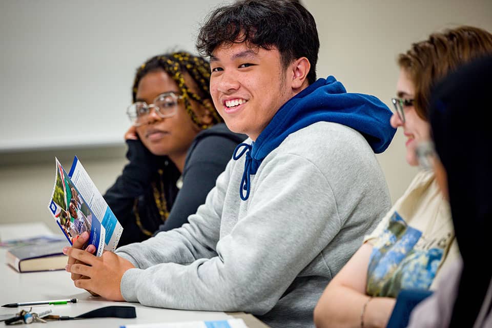 Students listen to their instructor while sitting at a desk in class.